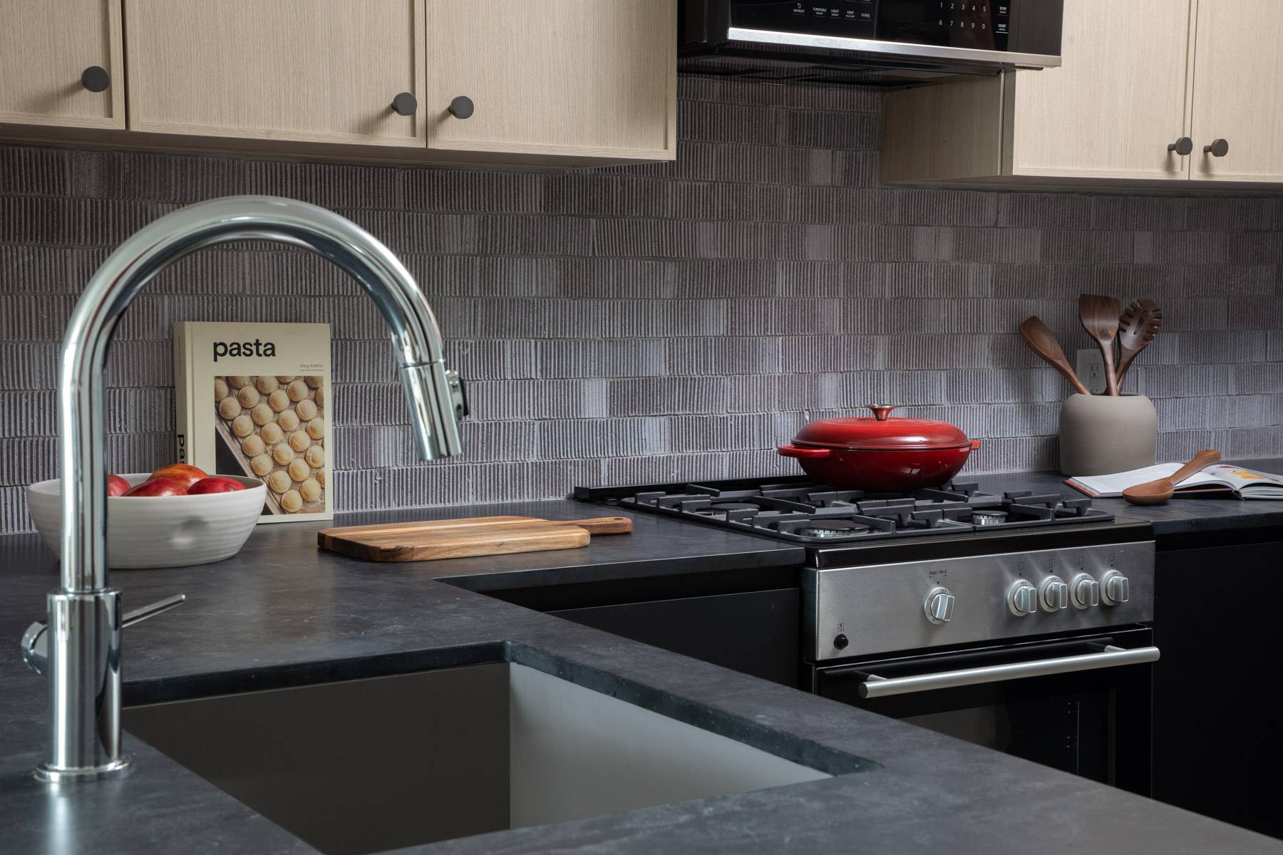 Kitchen detail showcasing flush square sink with chrome faucet, stainless steel and black stove, dark countertops and backsplash with light cabinets on top