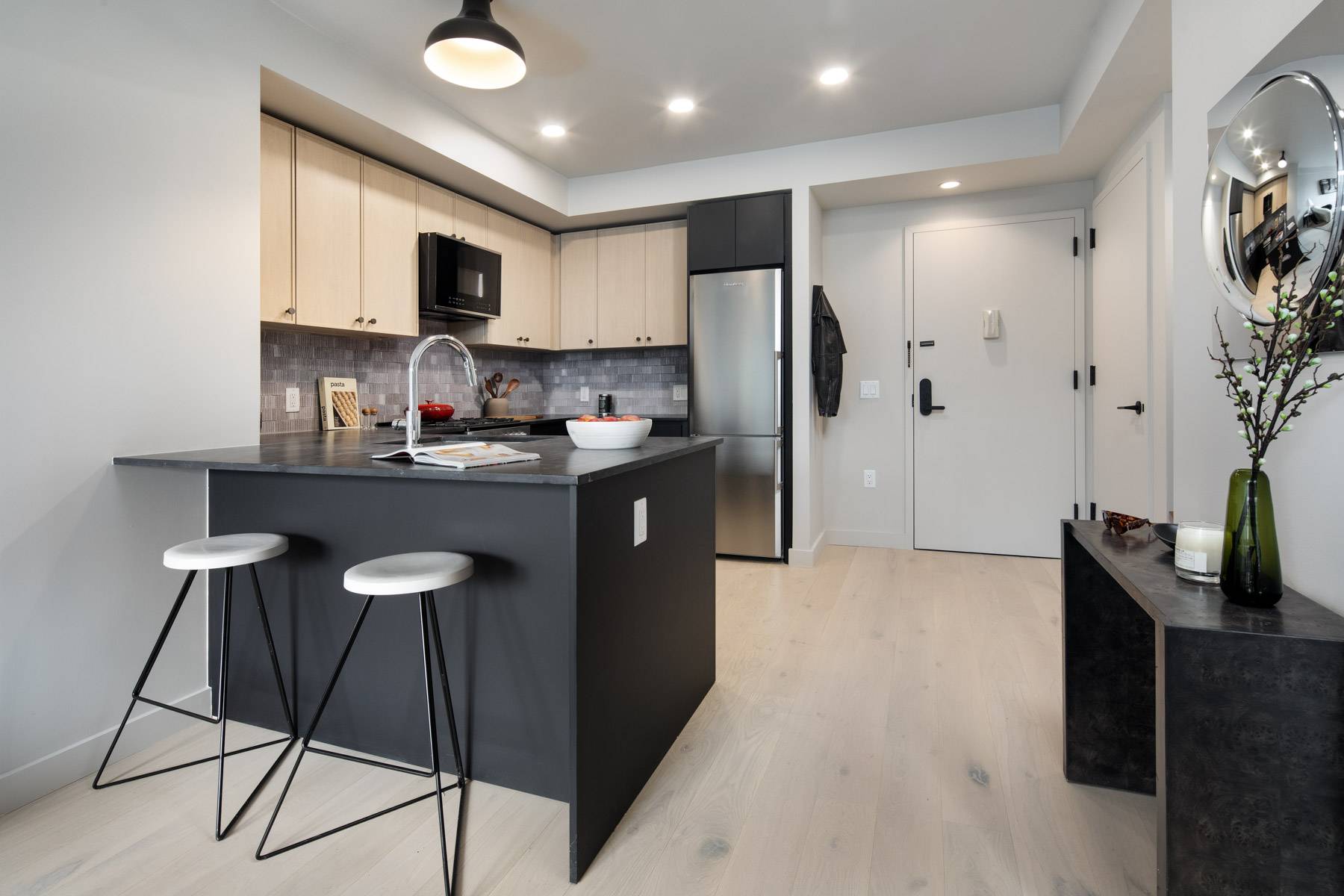 Chef inspired kitchen near entrance with dark eat in counter with stools, light flooring, light cabinetry on top, gray tone backsplash and stainless steel fridge